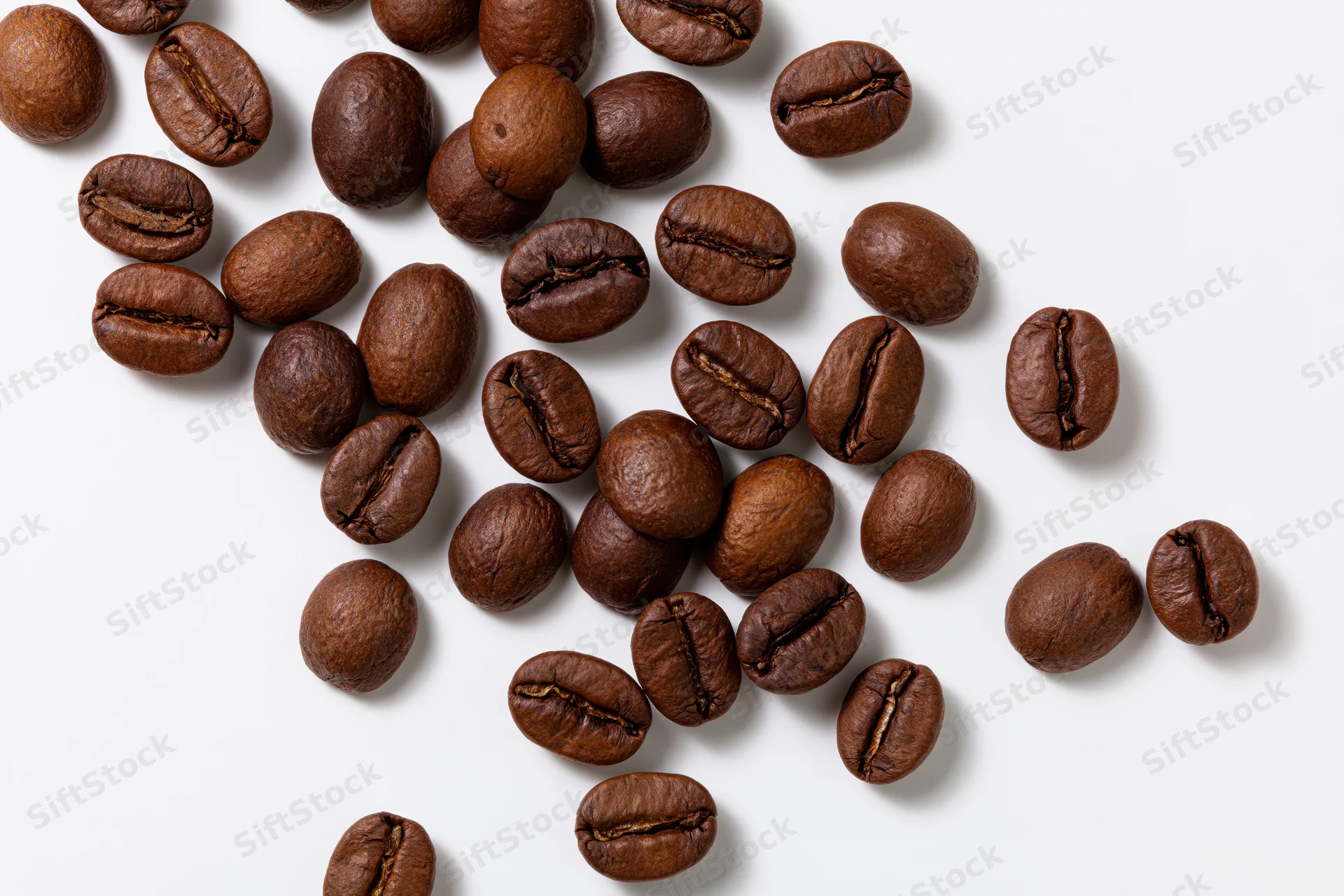 Roasted coffee beans scattered across a white flat surface in top view