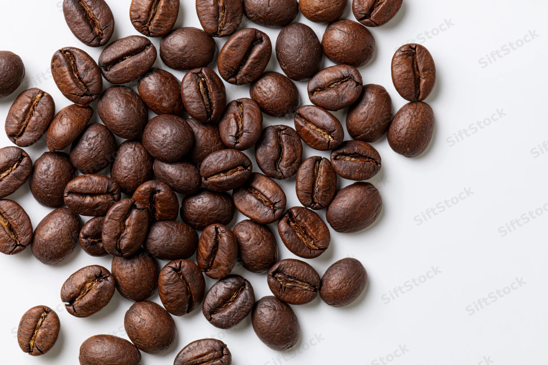 Roasted coffee beans scattered across a white surface with copyspace on the right