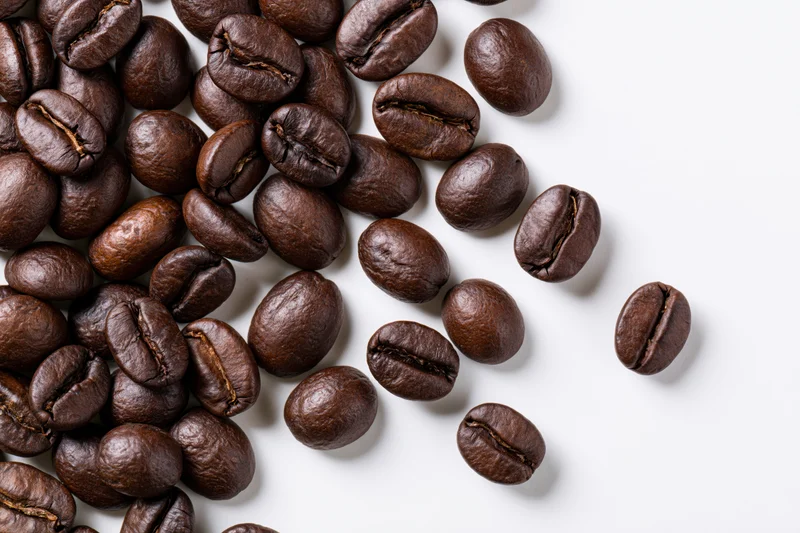 Roasted coffee beans scattered across a white surface in a flat lay arrangement