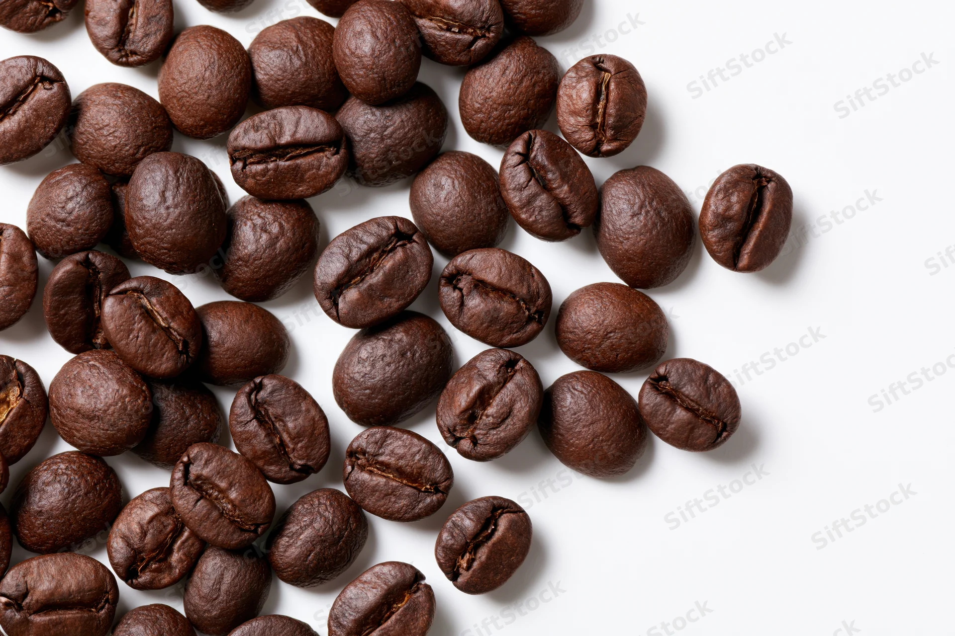 Roasted coffee beans scattered across a white surface with copyspace on the right