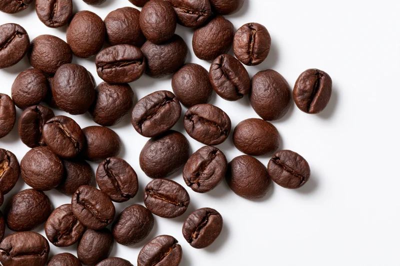 Roasted coffee beans scattered across a white surface with copyspace on the right