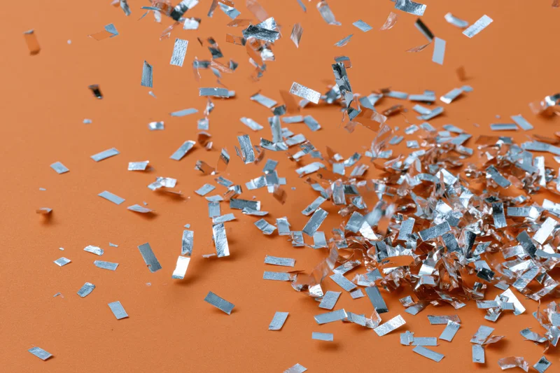 Silver metallic confetti pieces falling and scattered on an orange surface