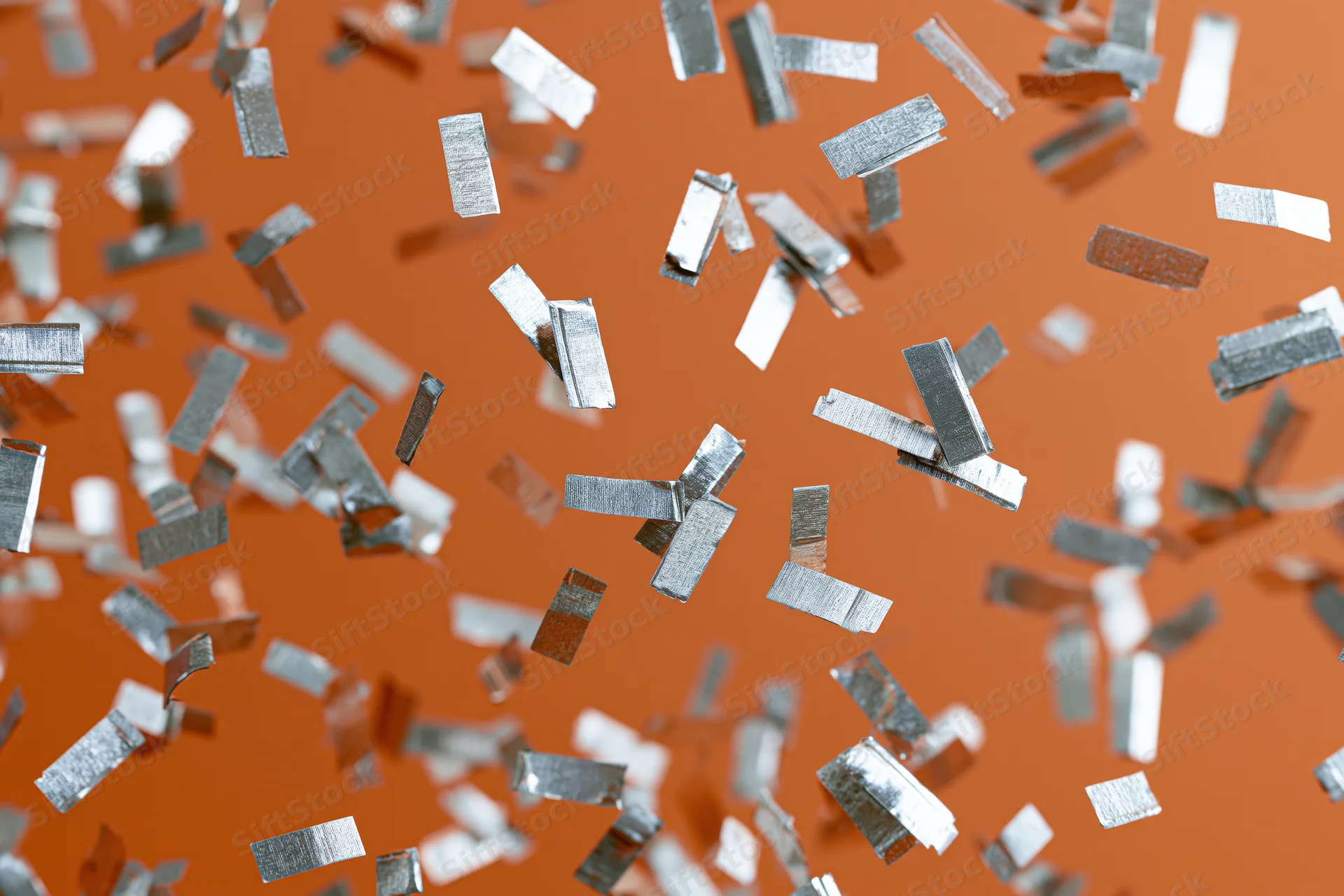Silver metallic confetti pieces falling mid-air against orange background