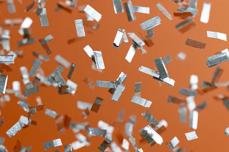 Silver metallic confetti pieces falling mid-air against orange background
