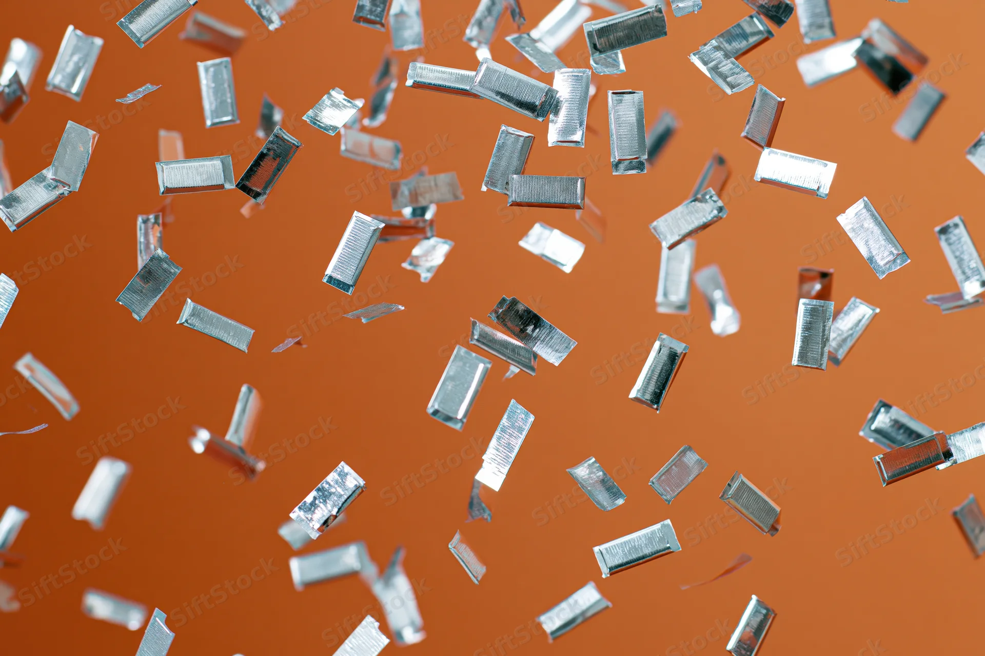 Silver metallic confetti pieces falling mid-air against orange background