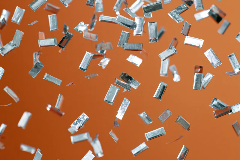 Silver metallic confetti pieces falling mid-air against orange background