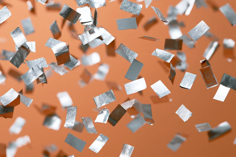 Silver metallic confetti pieces falling in mid-air against an orange background