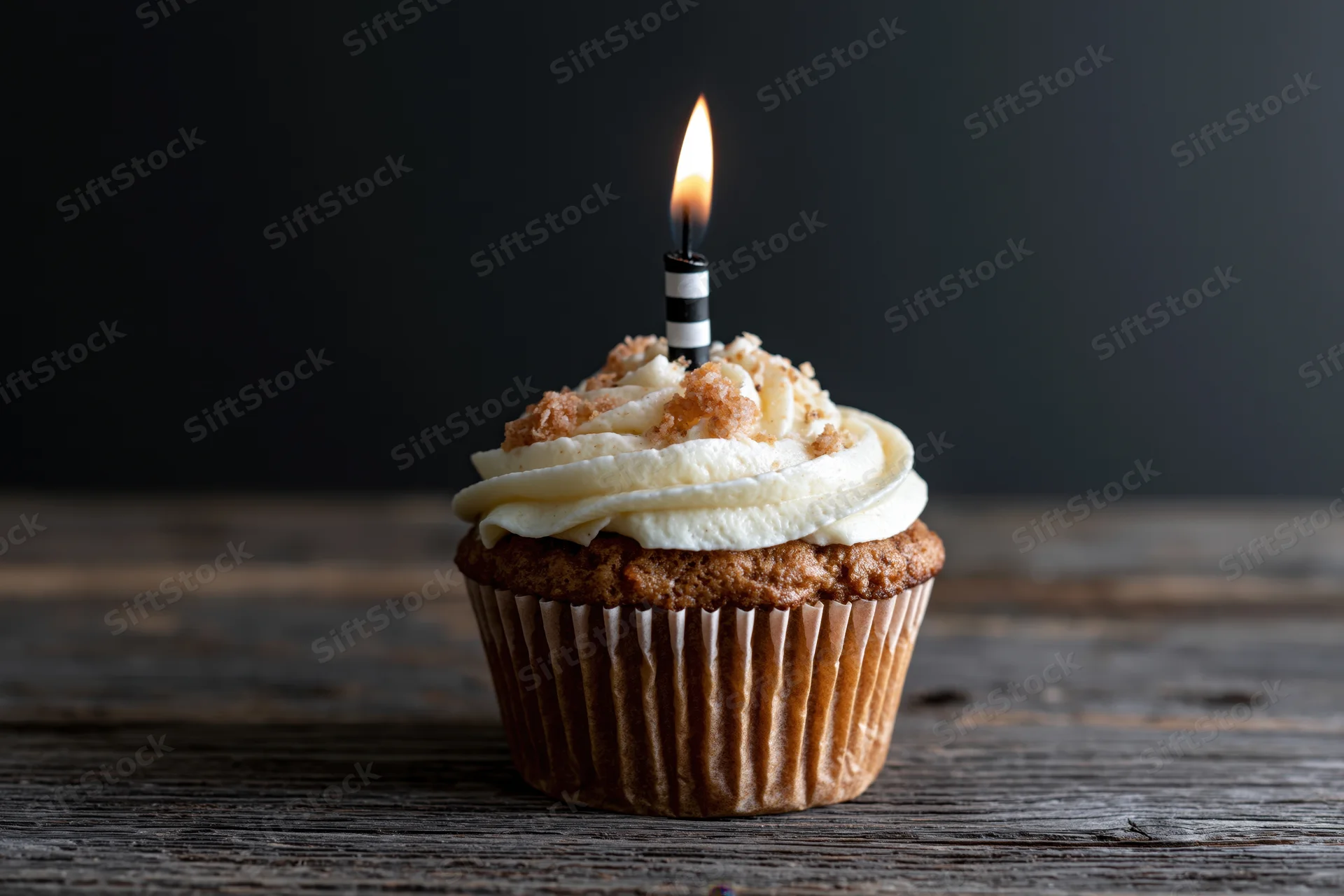 Single cupcake with white swirled frosting and lit candle on wooden table