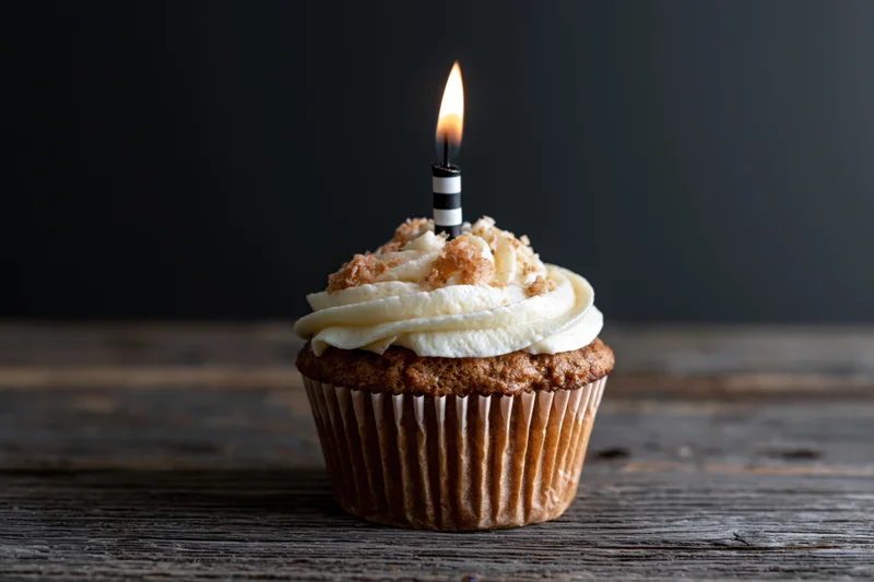 Single cupcake with white swirled frosting and lit candle on wooden table
