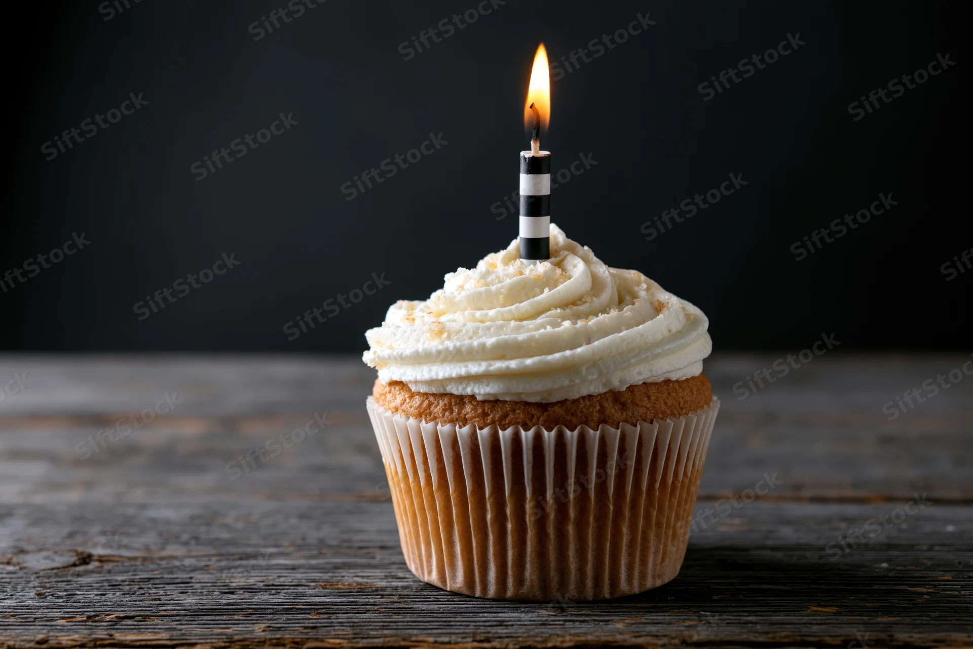Single cupcake with white swirled frosting and lit candle on wooden table