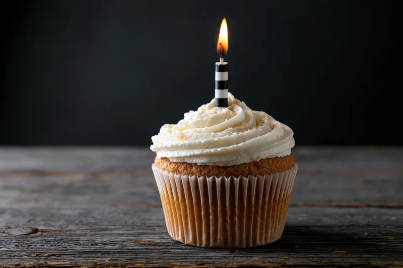 Single cupcake with white swirled frosting and lit candle on wooden table
