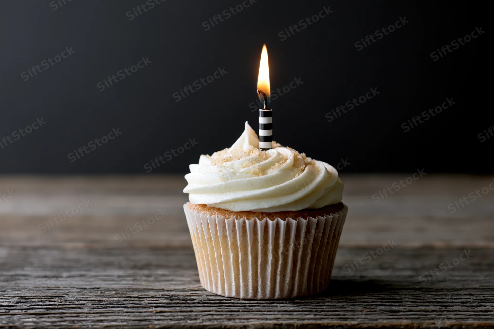 Single cupcake with white swirled frosting and lit candle on wooden table