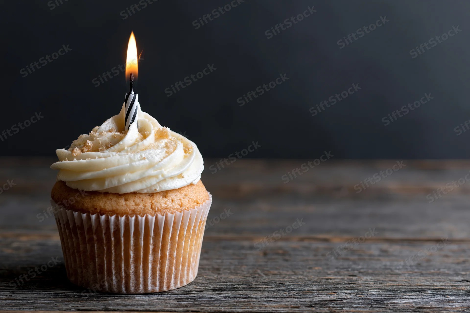 Single cupcake with white swirled frosting and lit candle on wooden table