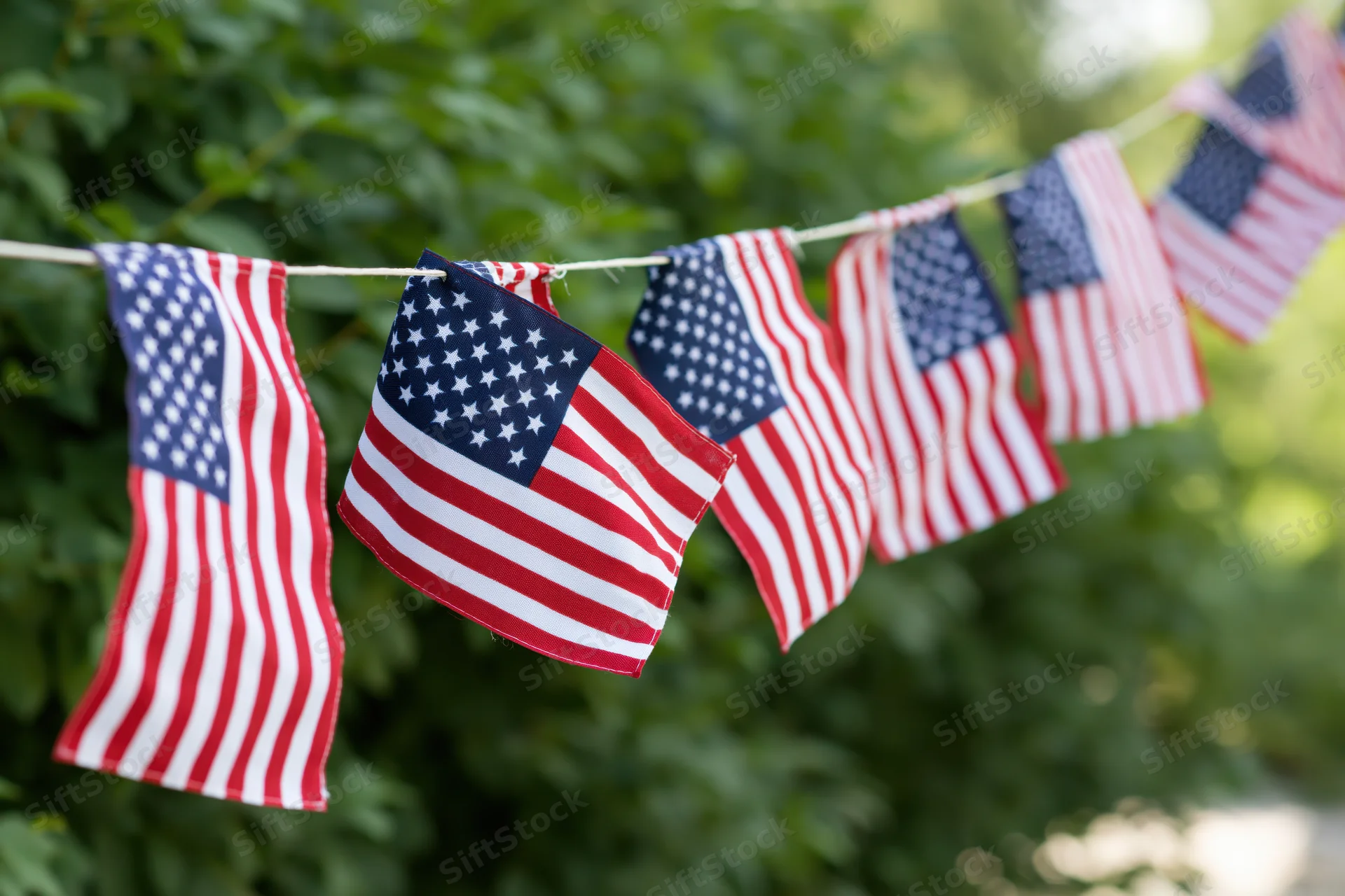 Small american flags strung as bunting hanging outdoors among green foliage