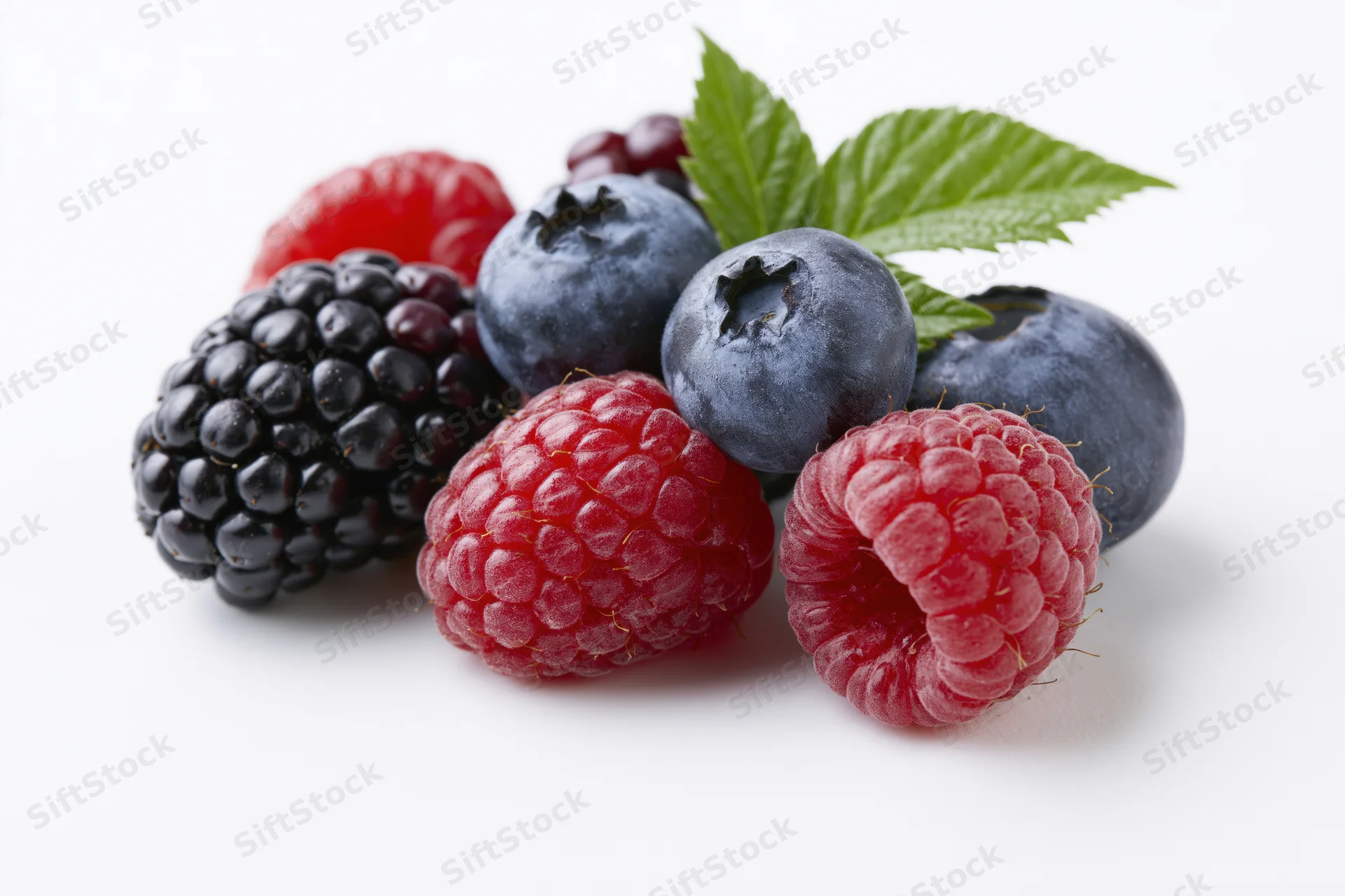 Cluster of fresh mixed berries including blackberries, raspberries and blueberries with a green leaf on white background