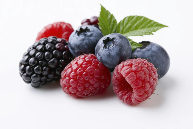 Cluster of fresh mixed berries including blackberries, raspberries and blueberries with a green leaf on white background
