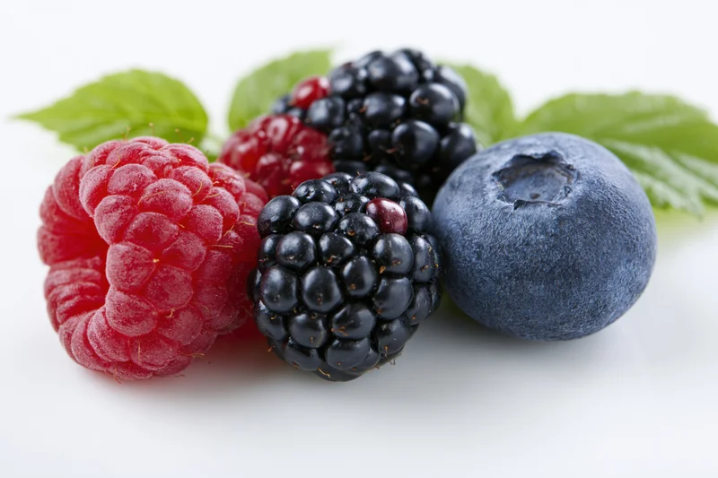 Fresh raspberry, blackberries and blueberry with green leaves on white background