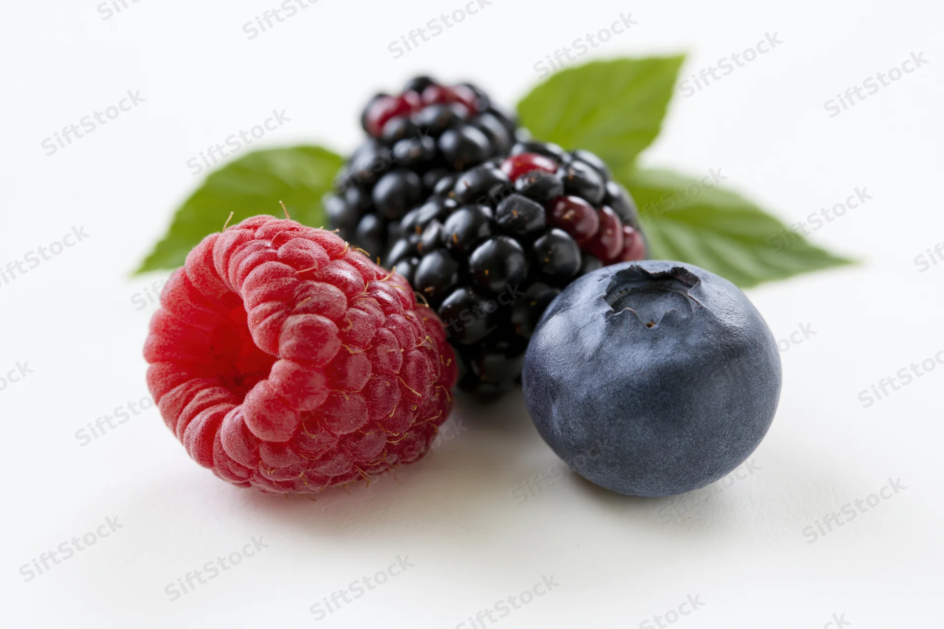 Raspberry, blackberries and blueberry arranged with green leaves on white background