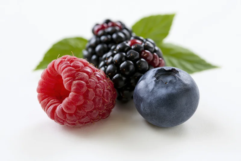 Raspberry, blackberries and blueberry arranged with green leaves on white background
