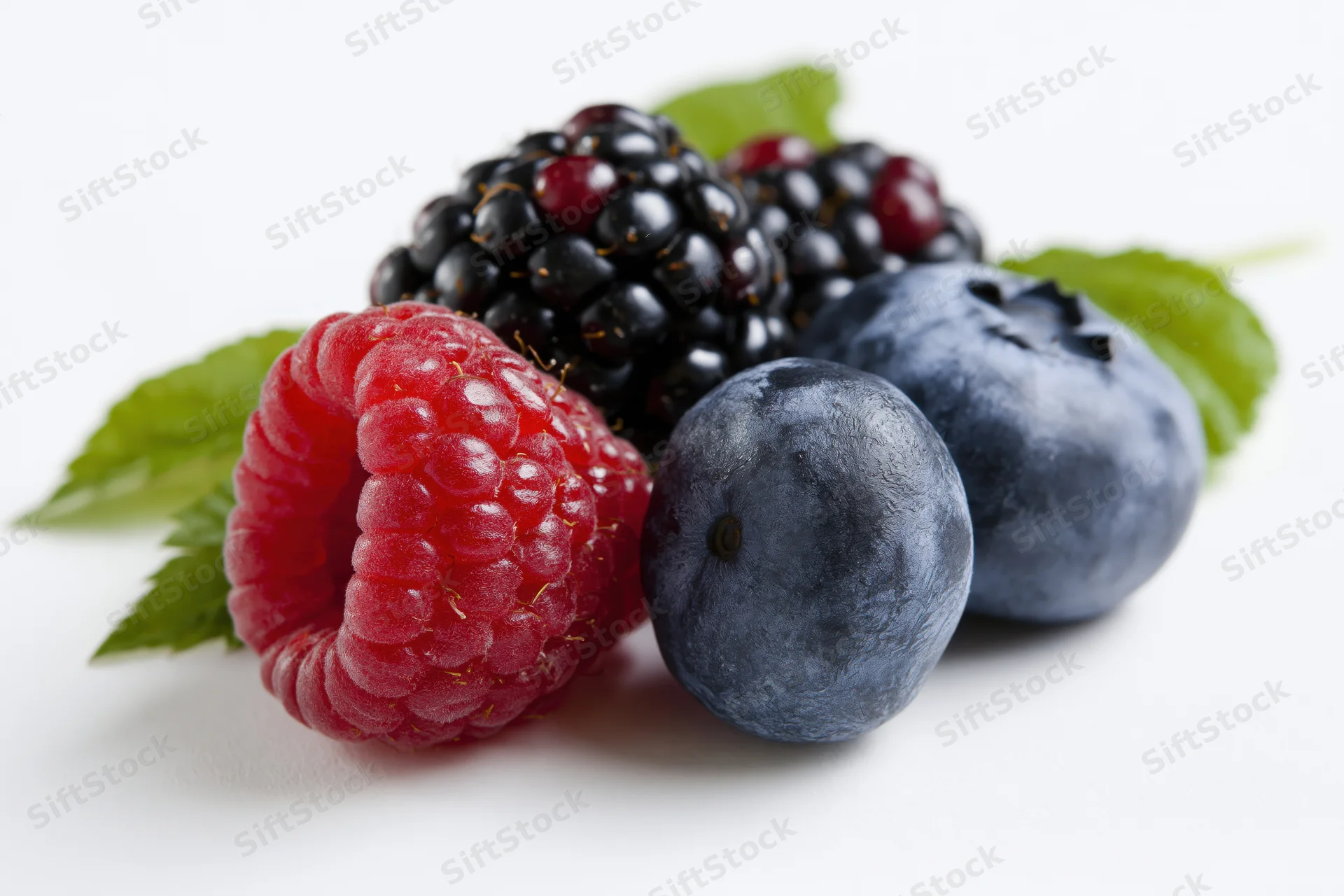 Fresh raspberry, blackberries and blueberries with green leaves on white background