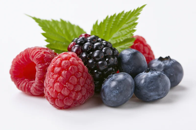 Mixed fresh berries arranged in a cluster with green leaves on white background