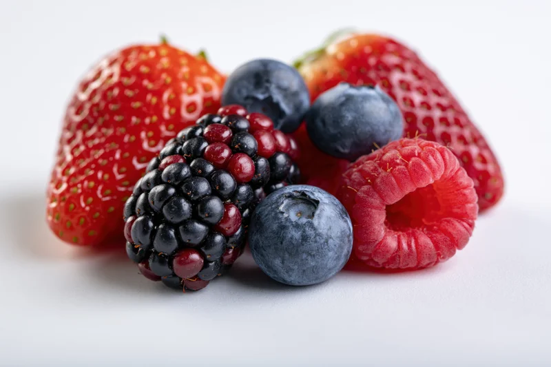 Mixed fresh berries including strawberry, blueberry, blackberry and raspberry arranged on white surface