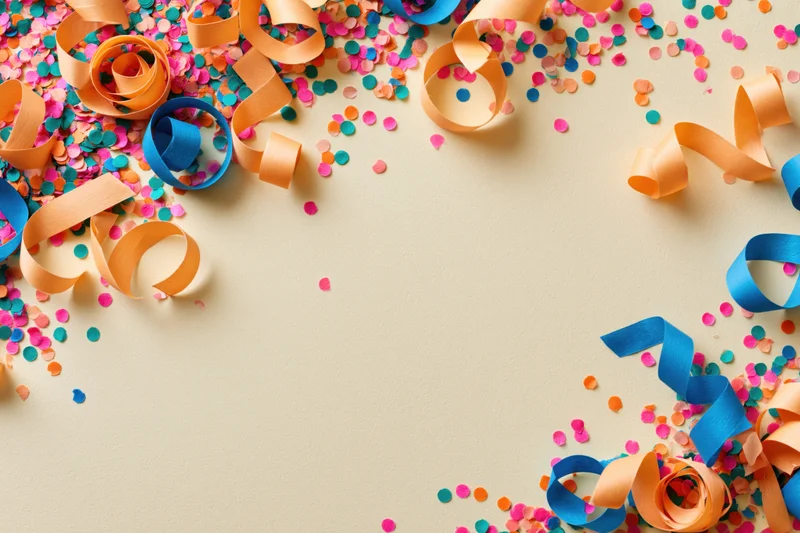Colorful paper confetti and curled ribbons scattered on beige surface with copyspace