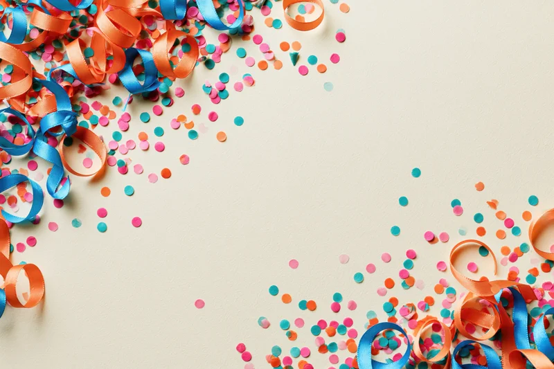 Colorful paper confetti and curled ribbons scattered on a light surface with copyspace