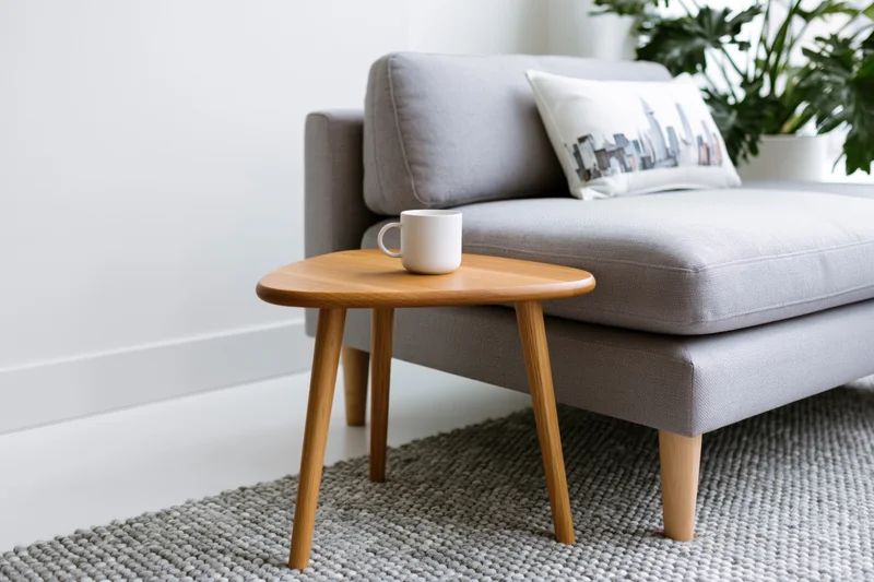 Small wooden side table with white ceramic mug beside gray sofa in living room