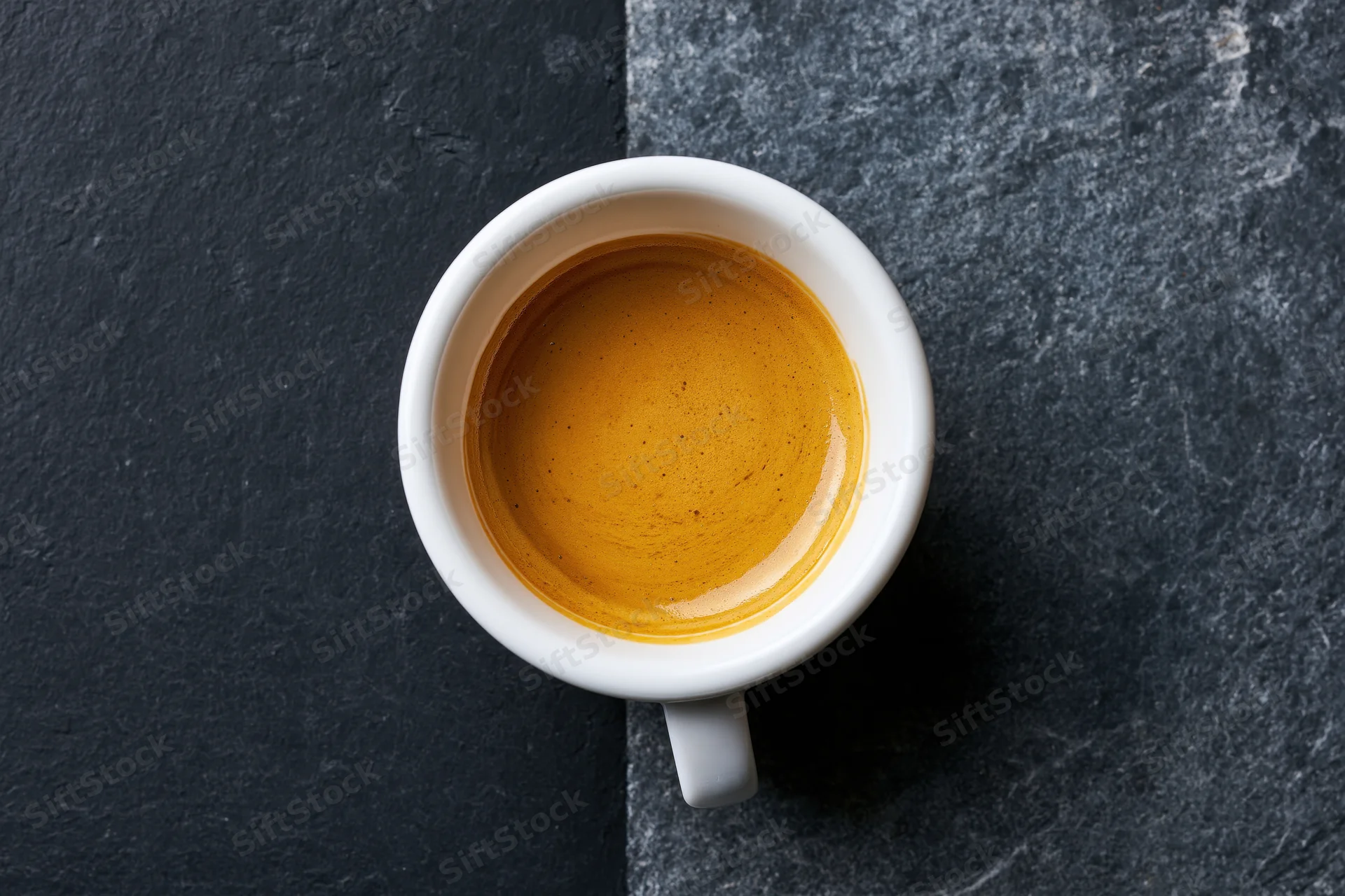 White ceramic espresso cup filled with golden-brown crema on dark stone surface, top view