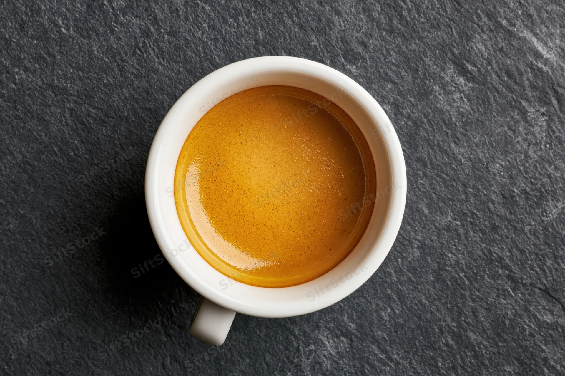 White ceramic espresso cup filled with golden-brown crema on dark slate surface, top view