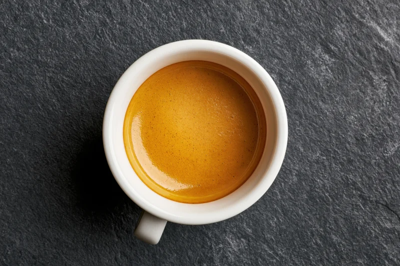 White ceramic espresso cup filled with golden-brown crema on dark slate surface, top view