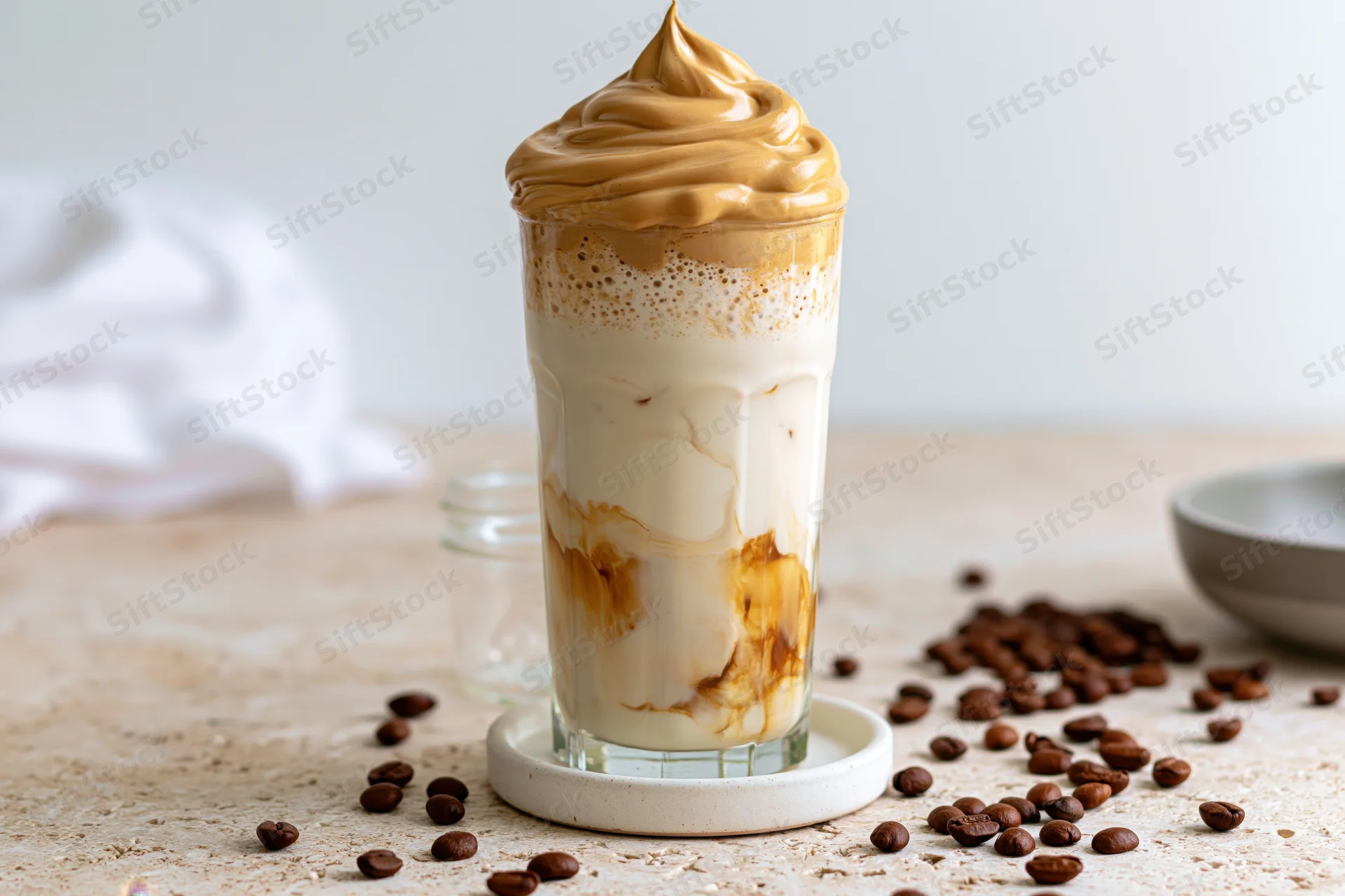 Tall glass of dalgona iced coffee with whipped cream swirl on a table surrounded by coffee beans