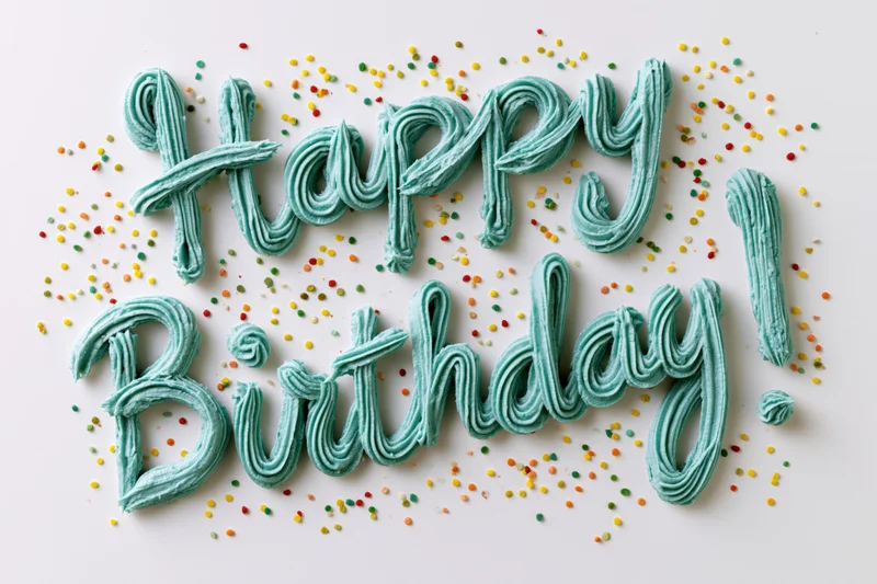 Teal buttercream frosting spelling happy birthday with colorful sprinkles on white surface