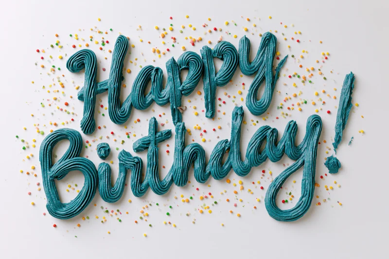 Teal buttercream frosting spelling happy birthday on white surface with colorful sprinkles scattered around