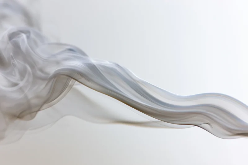 Thin wisps of grey smoke curling and drifting across a light background