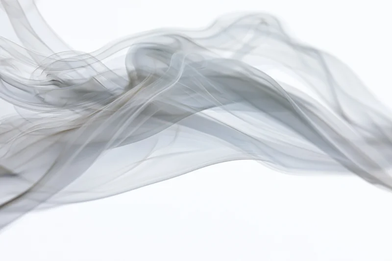 Thin gray smoke drifting and curling against a white background