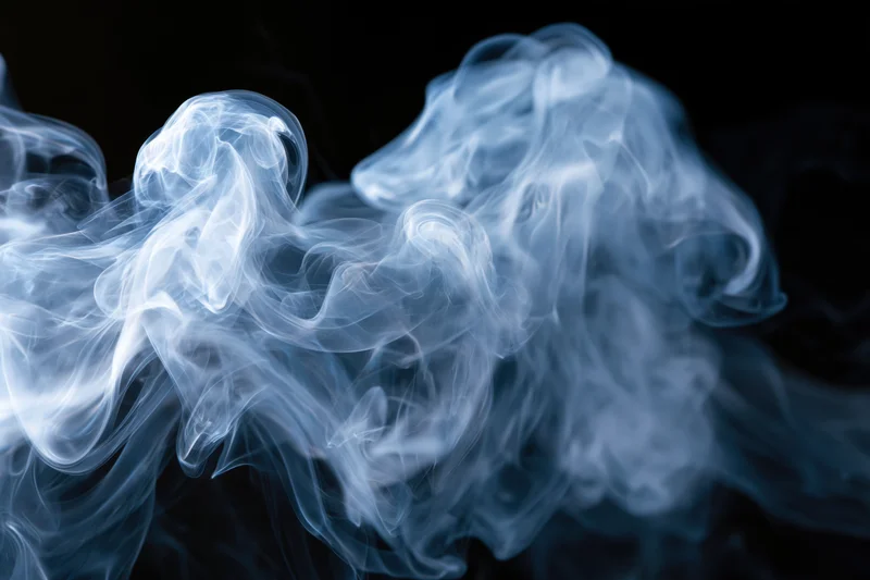 Thin wisps of smoke curling and billowing in midair against a black background