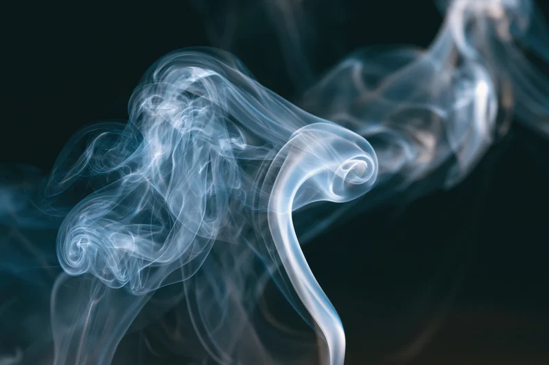 Thin wisps of smoke curling and billowing in midair against a dark background