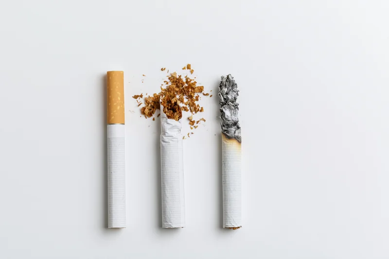 Three cigarettes arranged vertically on white background, one intact, one crushed, one burnt with ash