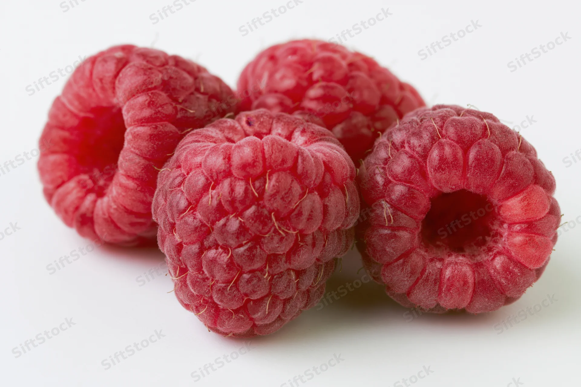 Four fresh raspberries clustered together on a white background