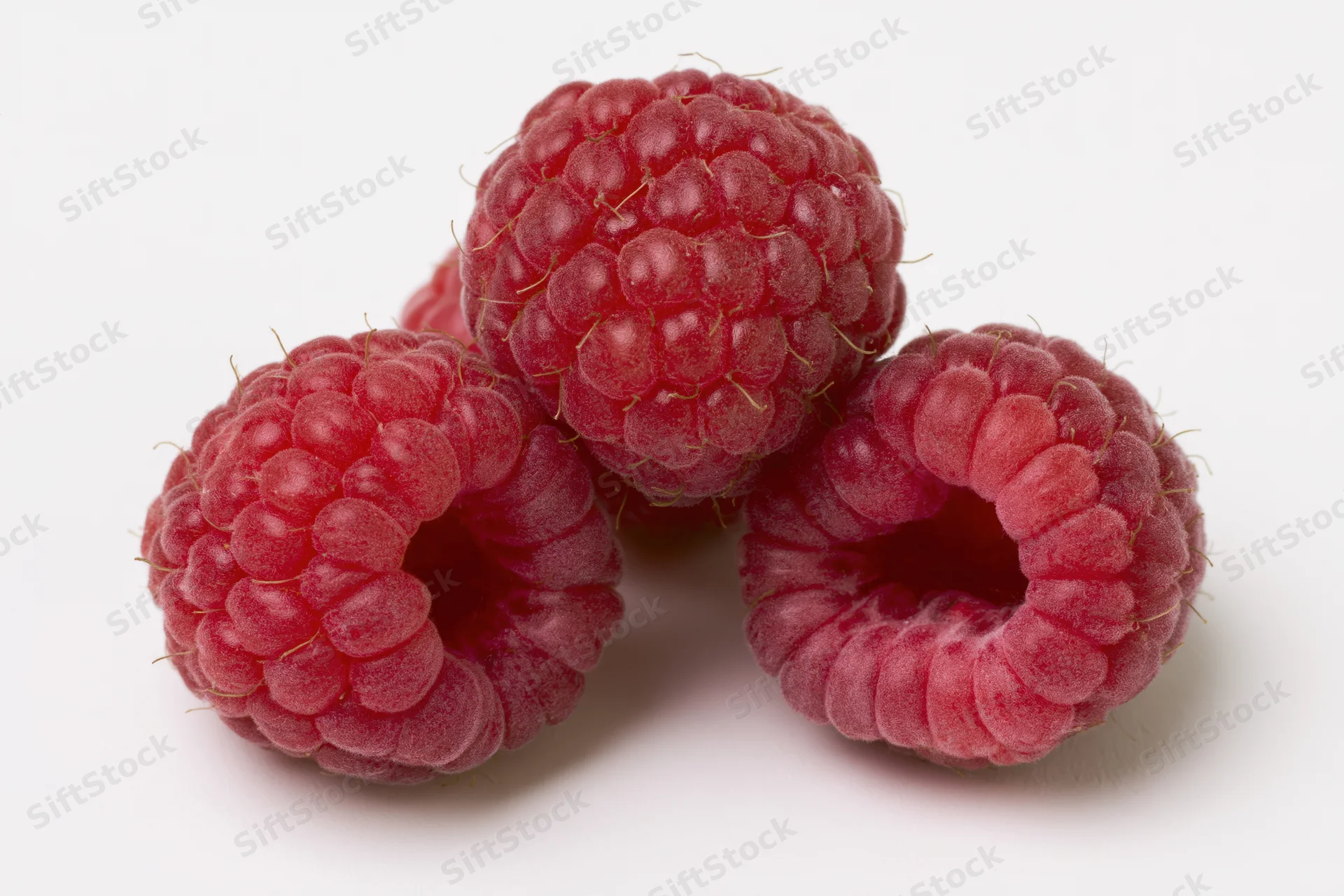 Three fresh raspberries clustered together on a white background