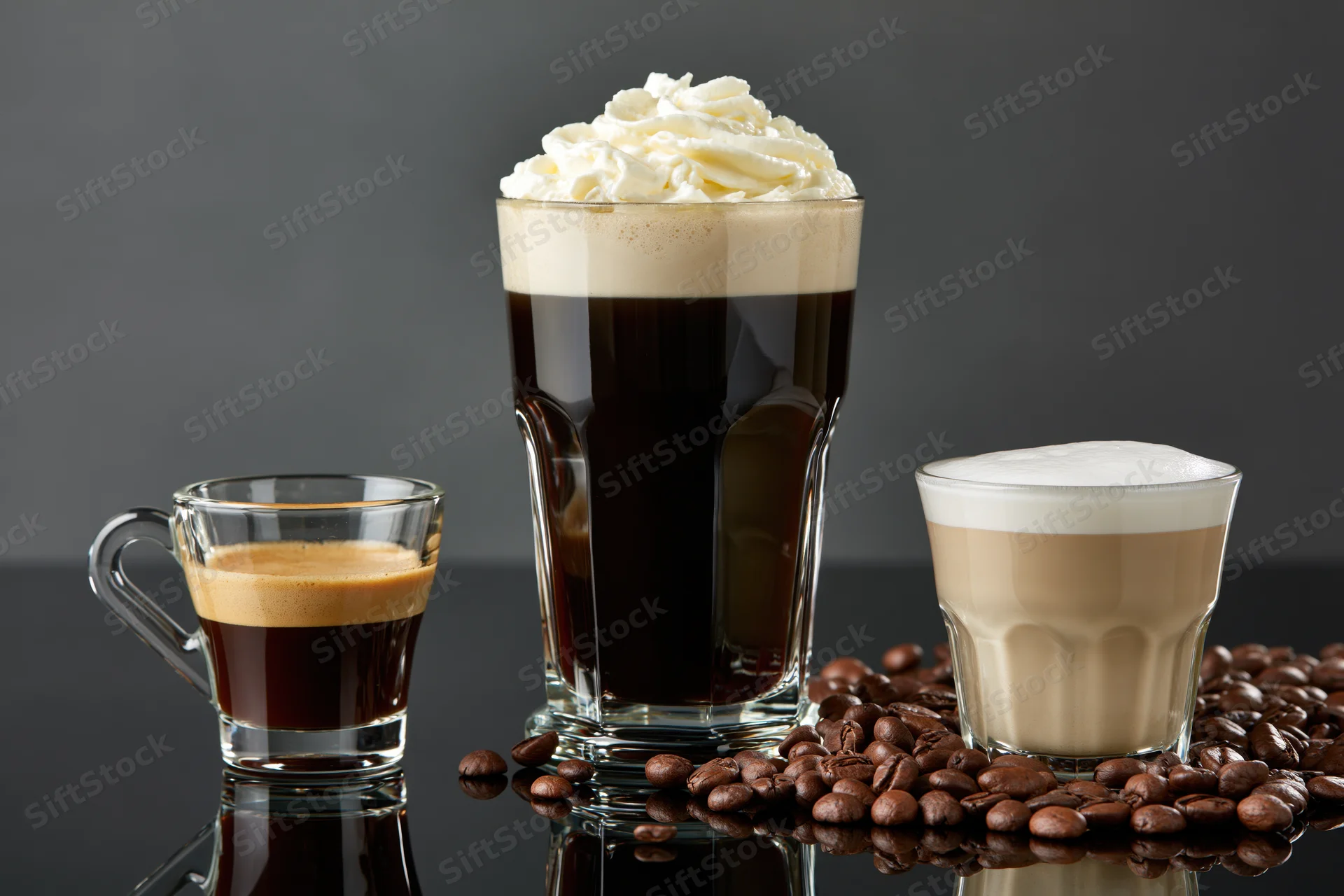Three glass coffee drinks arranged on a reflective black surface with coffee beans scattered around