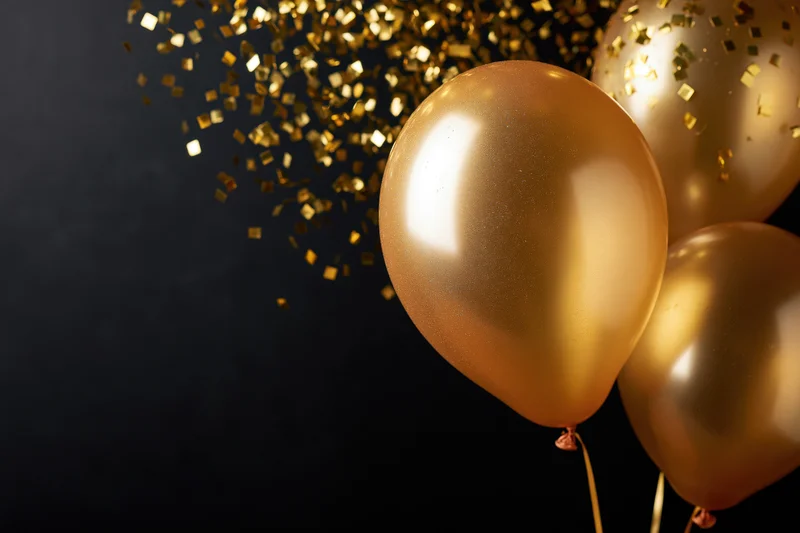 Glossy gold helium balloons floating with falling confetti against dark background