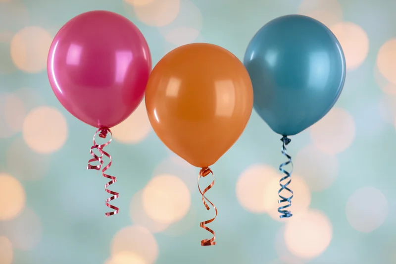 Three colorful latex balloons floating with curly ribbons against a soft bokeh background