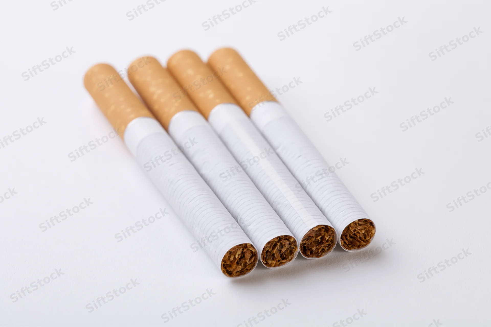 Four unlit cigarettes arranged in parallel on a white surface