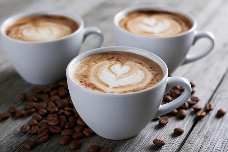Three white ceramic cups of latte art coffee arranged on a wooden table with scattered coffee beans