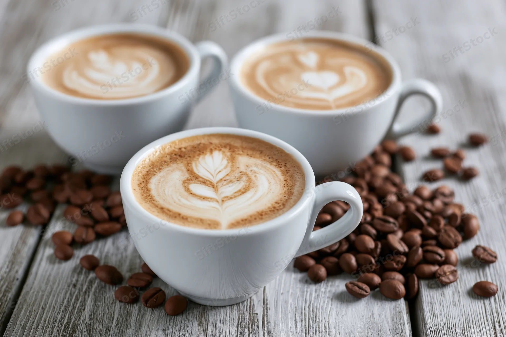 Three white ceramic cups of latte art coffee arranged on a wooden table with scattered coffee beans