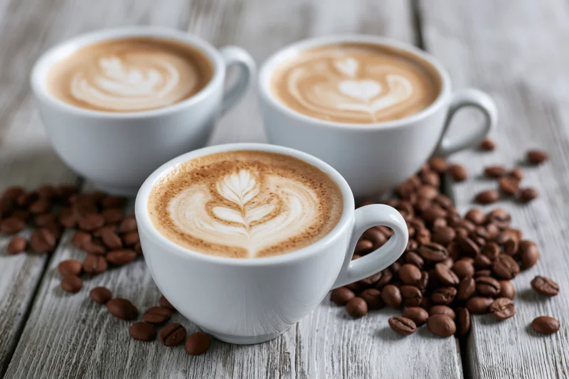 Three white ceramic cups of latte art coffee on wooden table