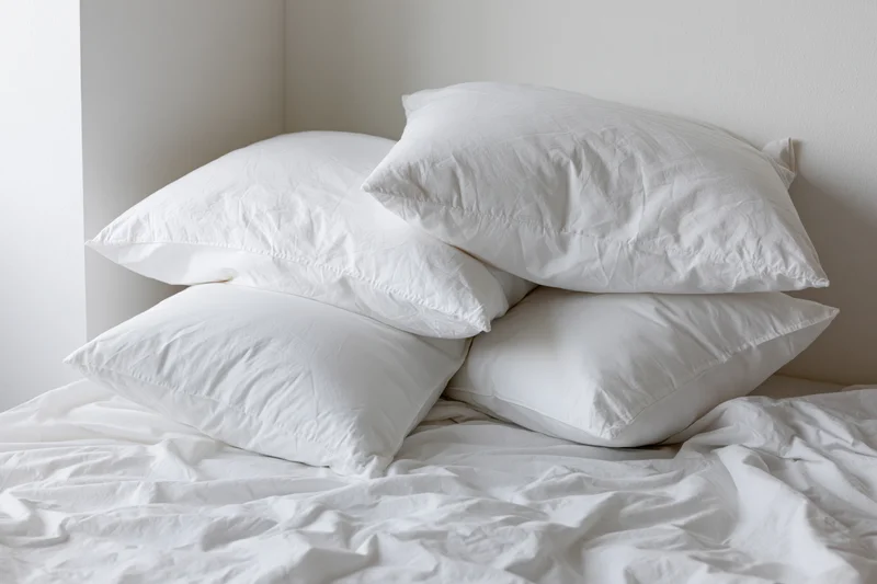 Four white pillows stacked on an unmade bed in a bedroom